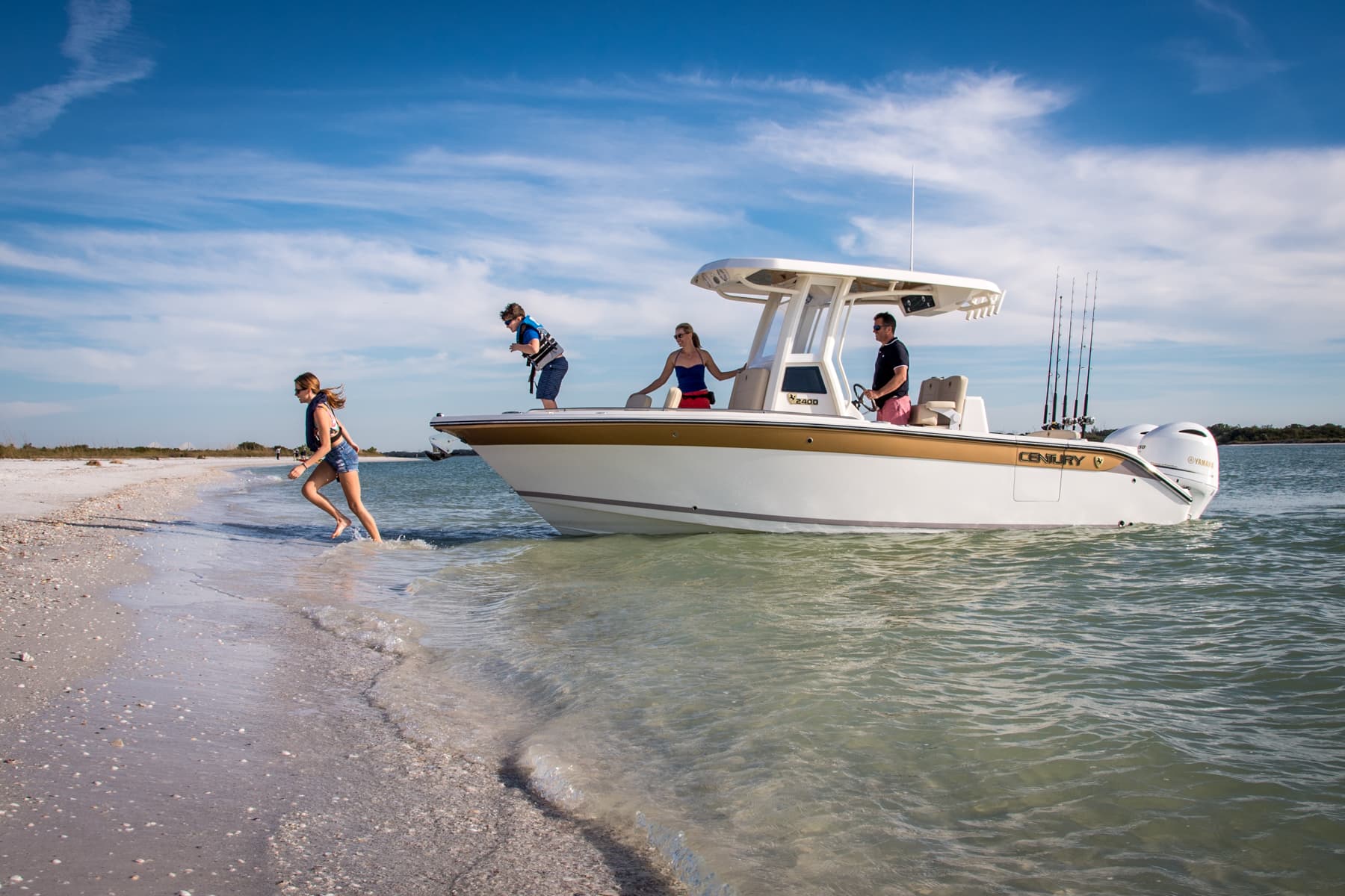 White center-console fishing boat with twin outboards at a sandy shoreline