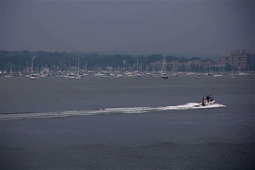 Small center-console boat speeding across a dark harbor under overcast skies